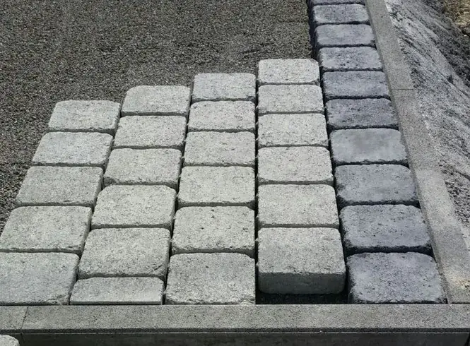 Betonpflaster beim Verlegen, an der Kante eine Zeile aus dunkleren Steinen