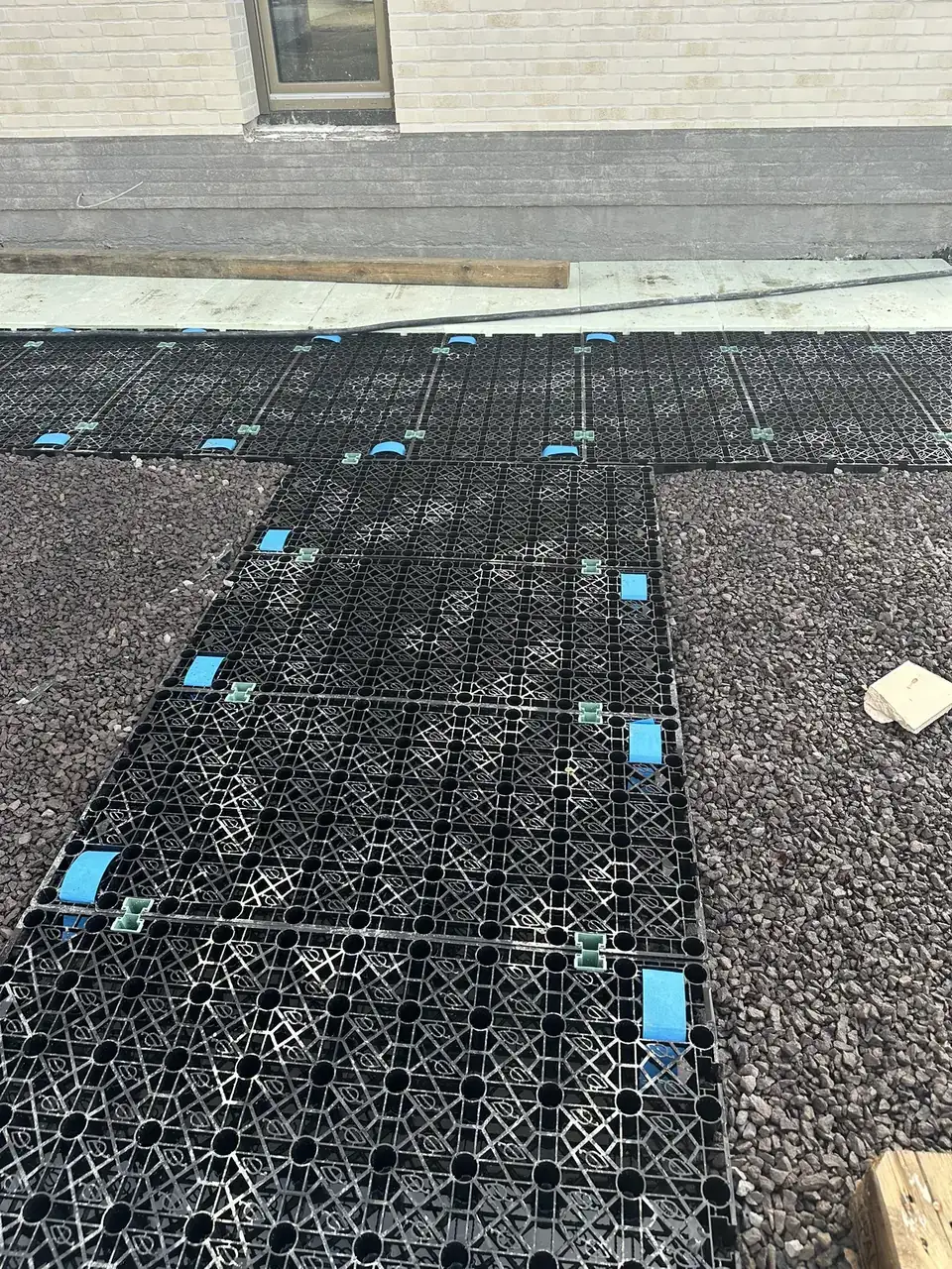 Verlegte Drän- und Retentionselemente aus schwarzem Kunststoff auf einem Flachdach, verbunden mit Steckverbindern, seitlich Kies