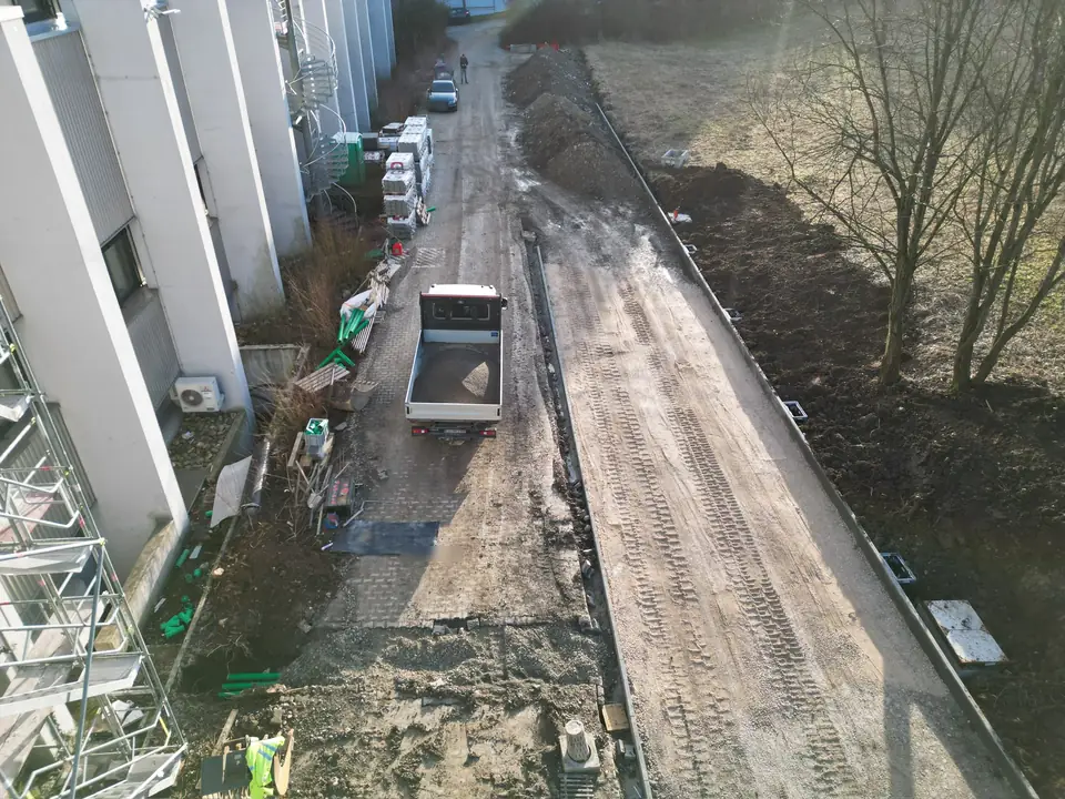 Langer Zufahrtsweg an einem Firmengebäude im Bau: Tragschicht, neue Randsteine, Abläufe und Pflasterpaletten