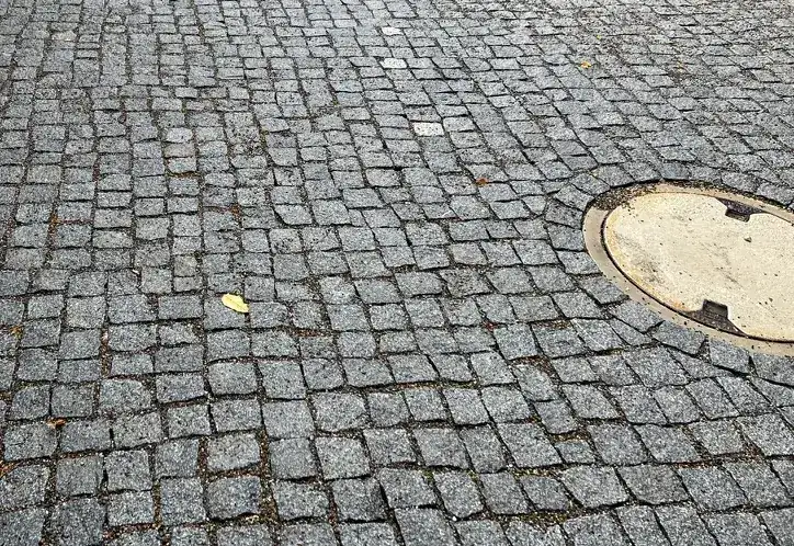 Granit-Kleinpflaster, sauber um einen runden Schachtdeckel gesetzt