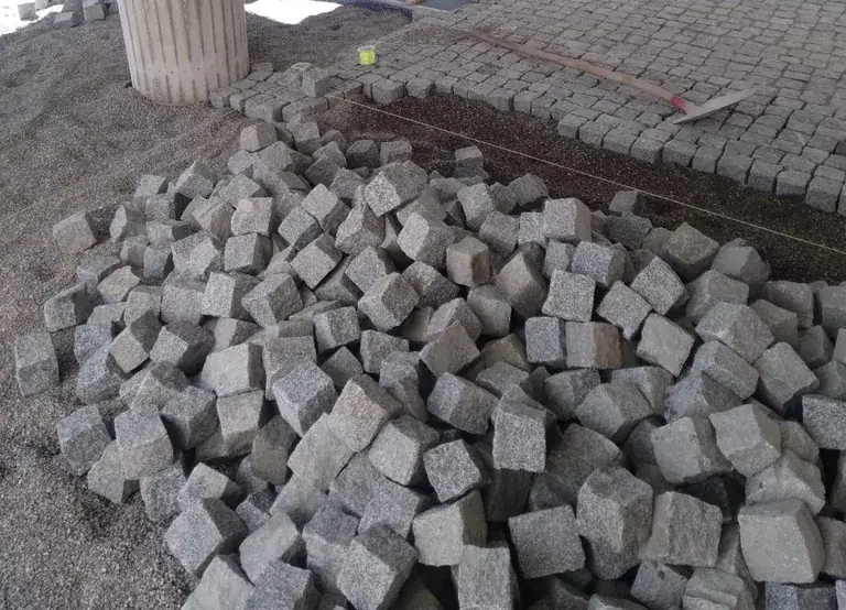 Haufen aus Granitsteinen vor einer Fläche, die gerade gepflastert wird