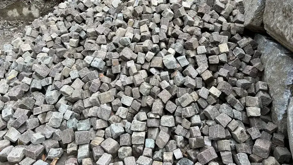 Frisch gelieferte Granitpflastersteine auf einem Haufen, daneben große Natursteinblöcke