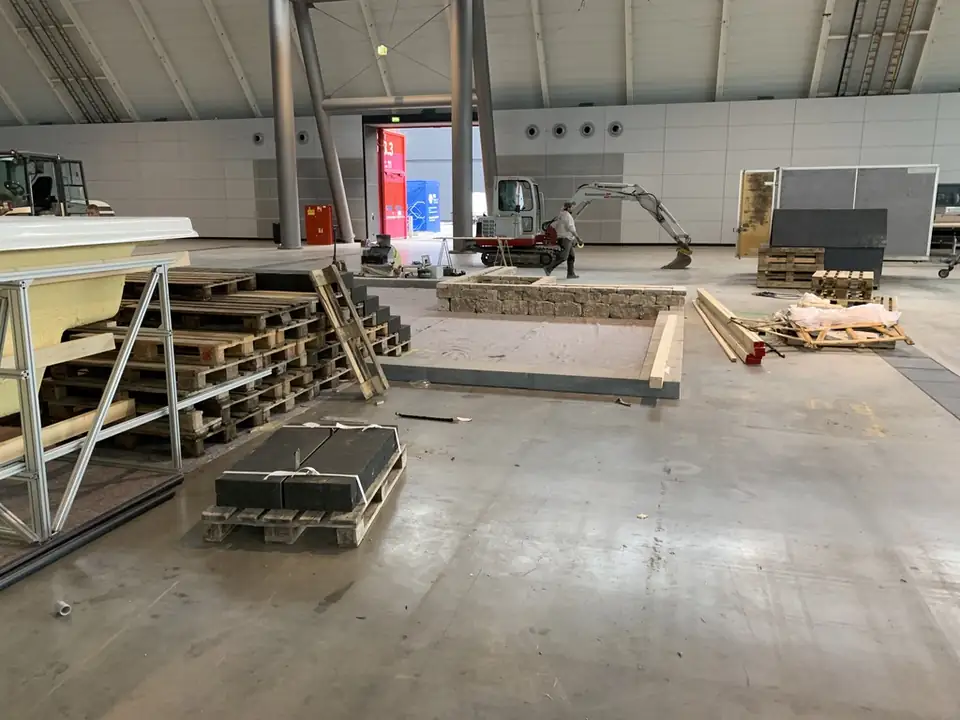 Aufbau in der Messehalle: Minibagger, Mauer aus Natursteinen und Paletten