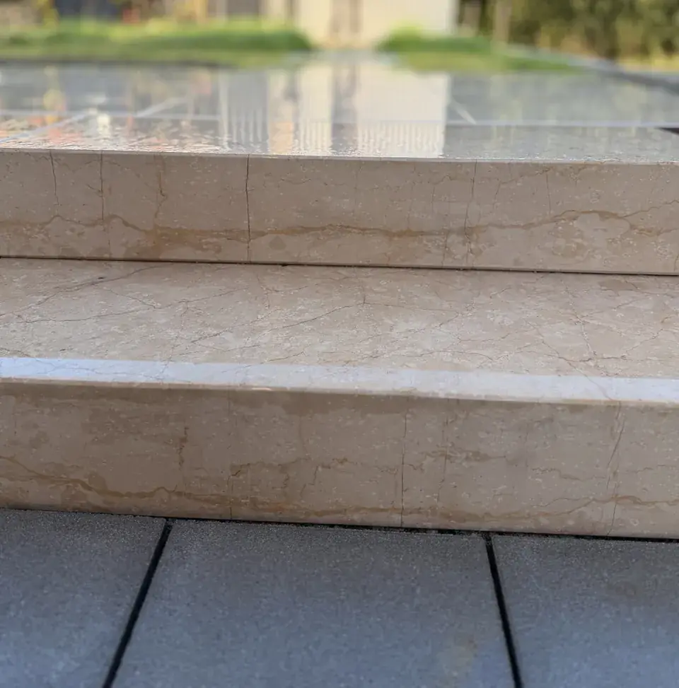 Zwei Blockstufen aus beigem Naturstein mit feinen Adern, dahinter die Terrasse aus Keramikplatten