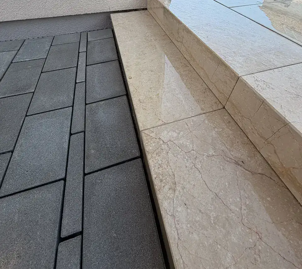 Seitlicher Blick auf beige Natursteinstufen neben dunklem Betonpflaster