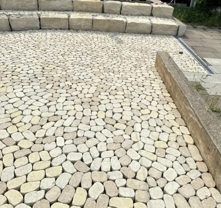 Zwei Reihen Sitzstufen aus hellen Blöcken Jurakalkstein vor einer Fläche aus gelbem Betonpflaster
