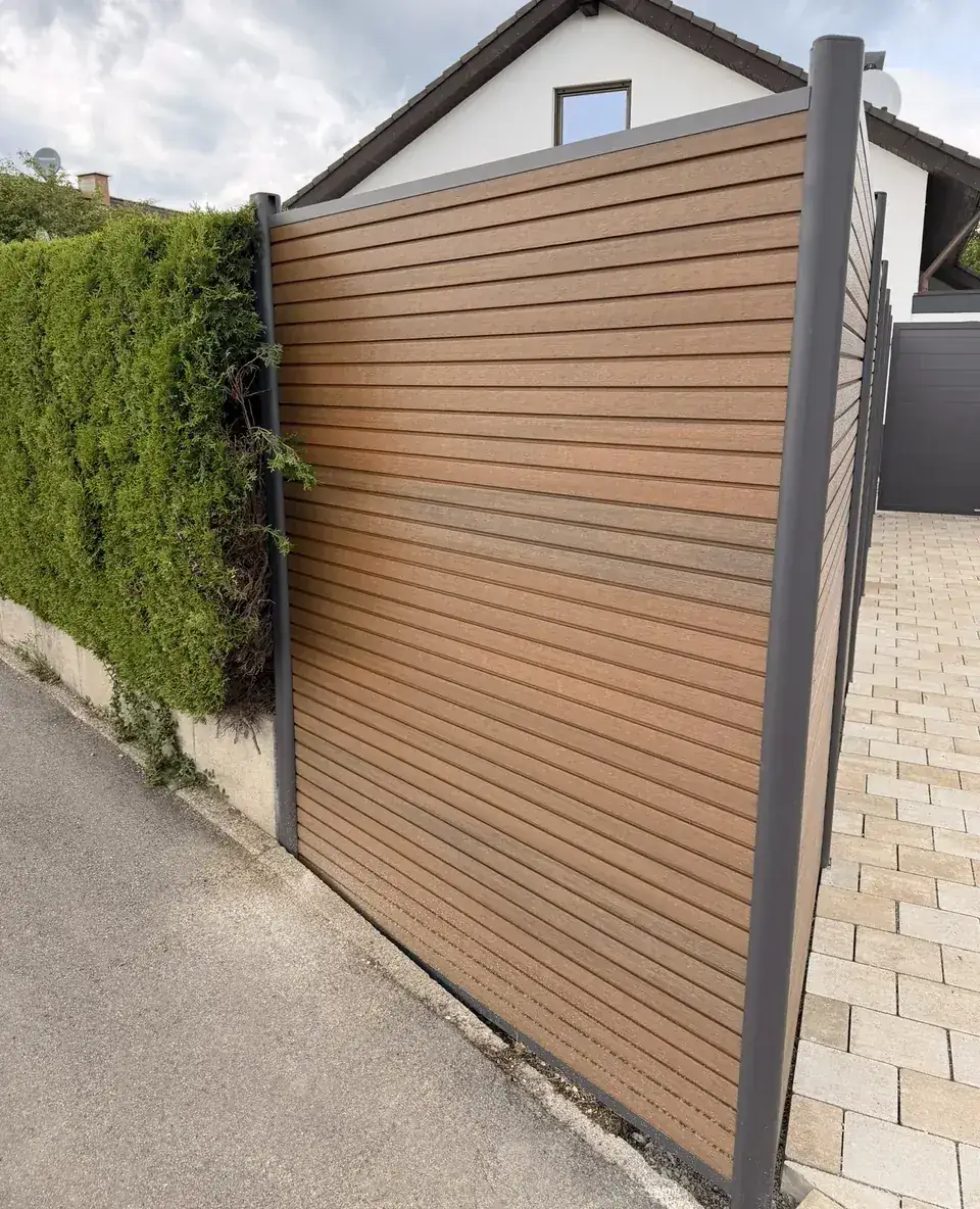 Sichtschutz aus WPC in Holzoptik an einer Grundstücksecke zwischen Gehweg und gepflasterter Einfahrt