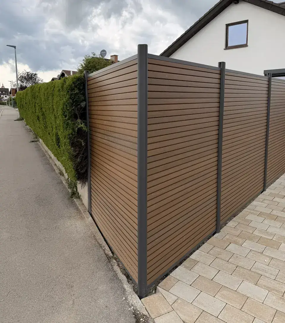 Langer Sichtschutz entlang eines Gehwegs, daneben eine Hecke