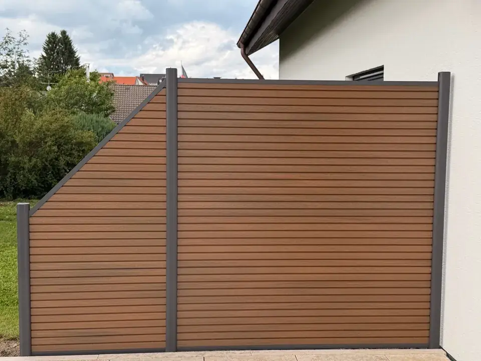 Sichtschutzwand aus WPC mit schräg abgestuftem Feld vor einem Garten