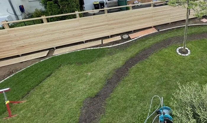 Sichtschutz aus Lärche, davor ein geschwungenes Pflanzbeet mit Mähkante aus Pflastersteinen im Rasen