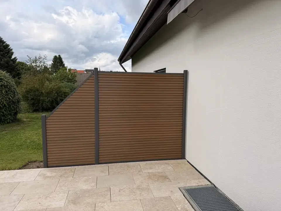 Sichtschutzwand aus WPC in Holzoptik mit anthrazitfarbenen Pfosten an einer Terrasse aus Natursteinplatten