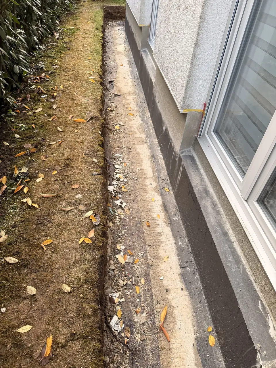 Abgedichteter Sockel entlang der Fenster, daneben der offene Graben vor dem Wiederherstellen