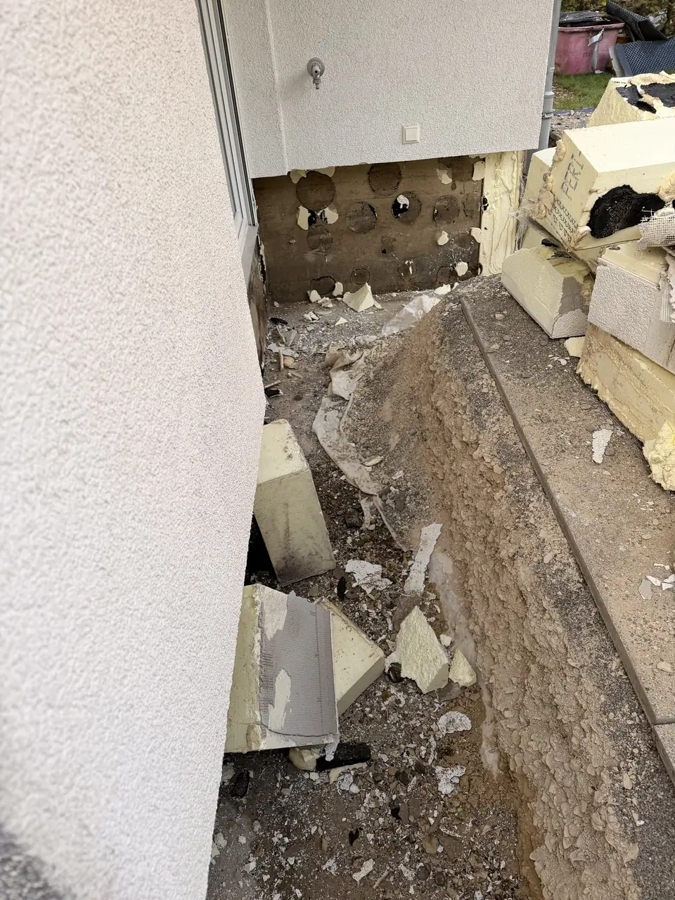 Freigelegter Sockel an einem Hausvorsprung, ausgebaute Dämmplatten liegen gestapelt daneben