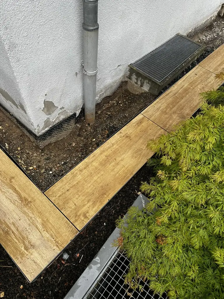 Freigelegter Gebäudesockel an einer Hausecke, davor Plattenweg und Pflanzbeet