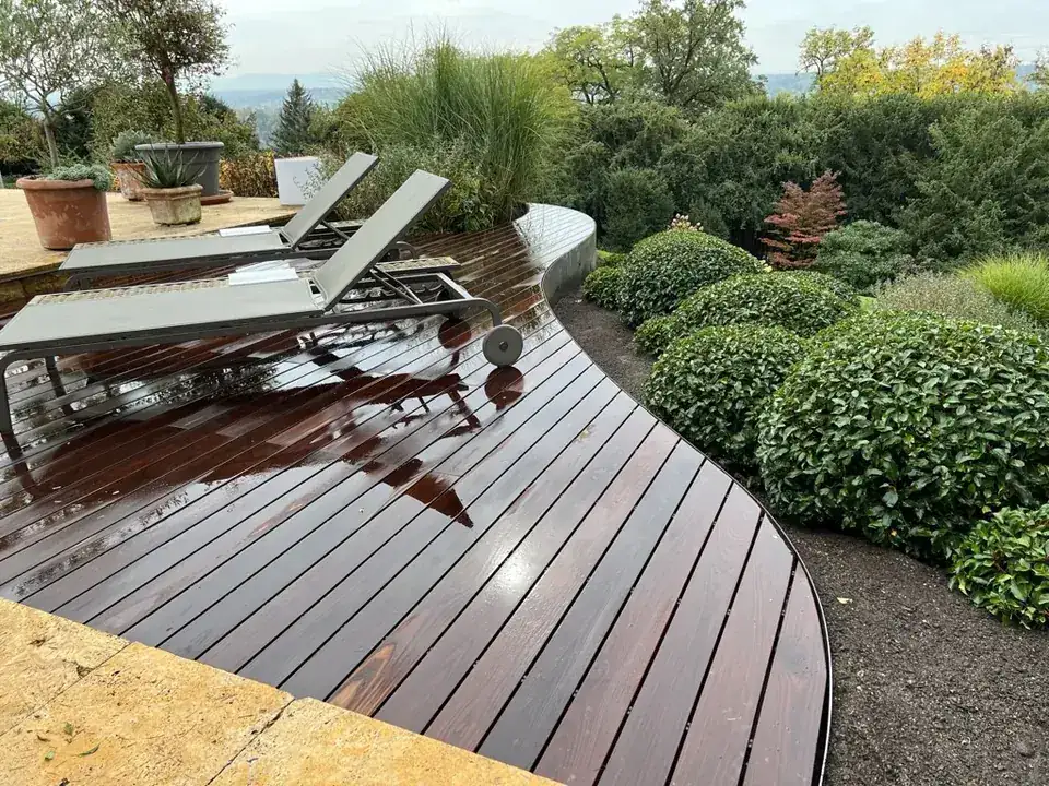 Geschwungene Holzterrasse aus Thermoesche mit Liegen, eingefasst von Kugelbuchs, Blick ins Tal