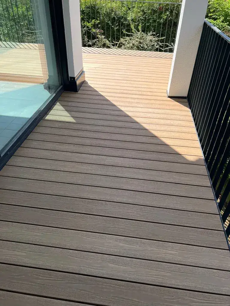 Fertig verlegte WPC-Dielen in Holzoptik auf einem Balkon mit Glasfront und dunklem Geländer